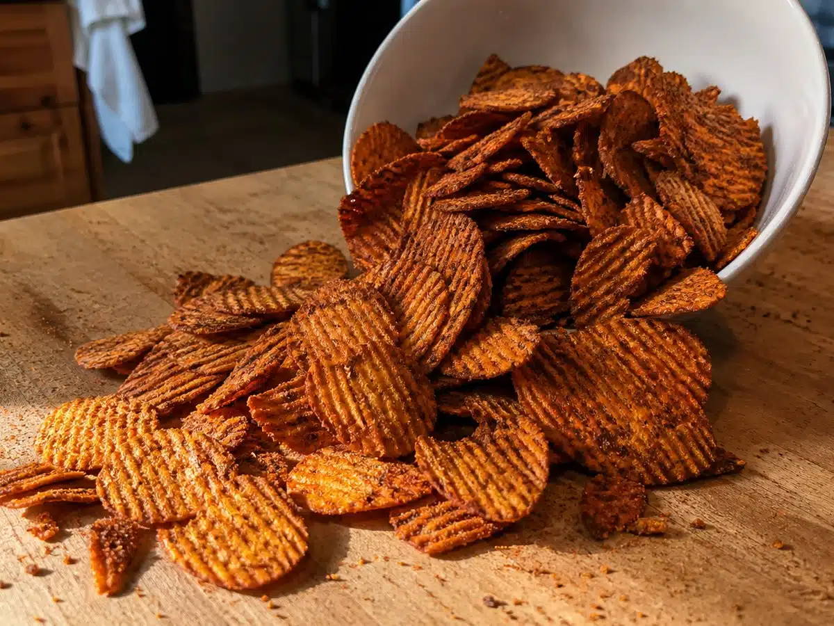 Barbecue potato chips spilling from a bowl onto a wooden counter